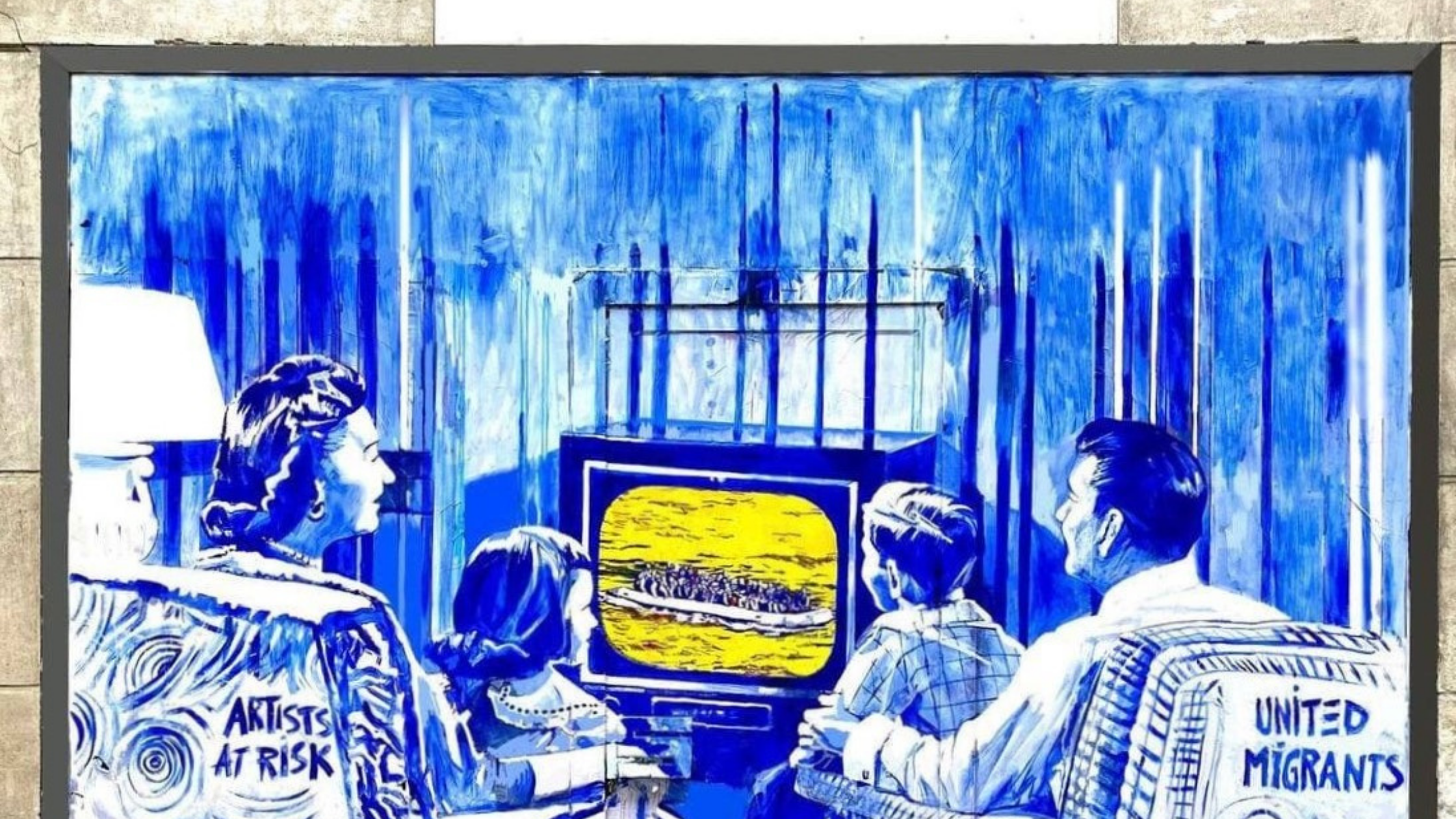 Mural on entrance to 210 House of Healing showing family of 4 sitting in armchairs watching TV. On tv is a boat with migrants. Armchairs have the words "Artists at Risk" and "United Migrants"